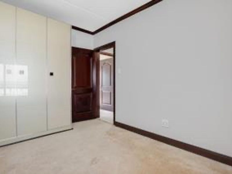 A clean, empty bedroom featuring neutral carpeting, built-in cupboards, and dark timber door frames, offering a blank canvas for personalization.