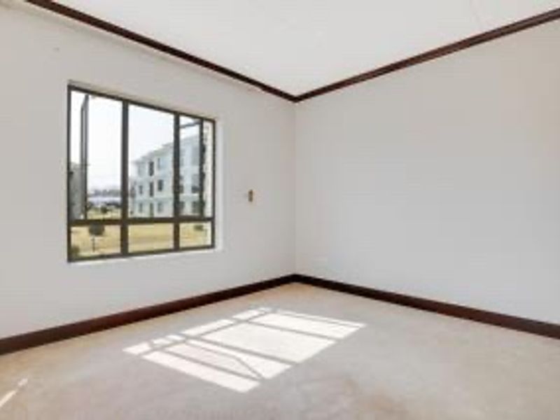 A bright, empty bedroom featuring neutral walls, dark trim detailing, and a large window providing natural light.