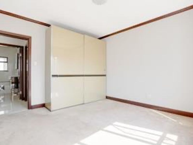 A bright, empty bedroom featuring a large built-in wardrobe, crown molding, and neutral carpeting, with an adjacent view into a bathroom.