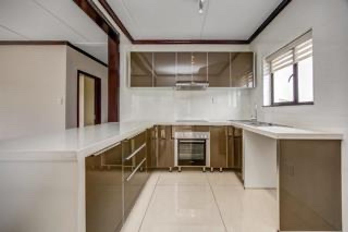 Modern kitchen featuring high-gloss cabinetry, built-in oven, extractor fan, and tiled flooring, offering a clean and functional workspace.