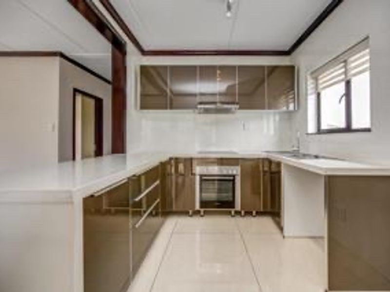 Modern kitchen featuring high-gloss cabinetry, built-in oven, extractor fan, and tiled flooring, offering a clean and functional workspace.