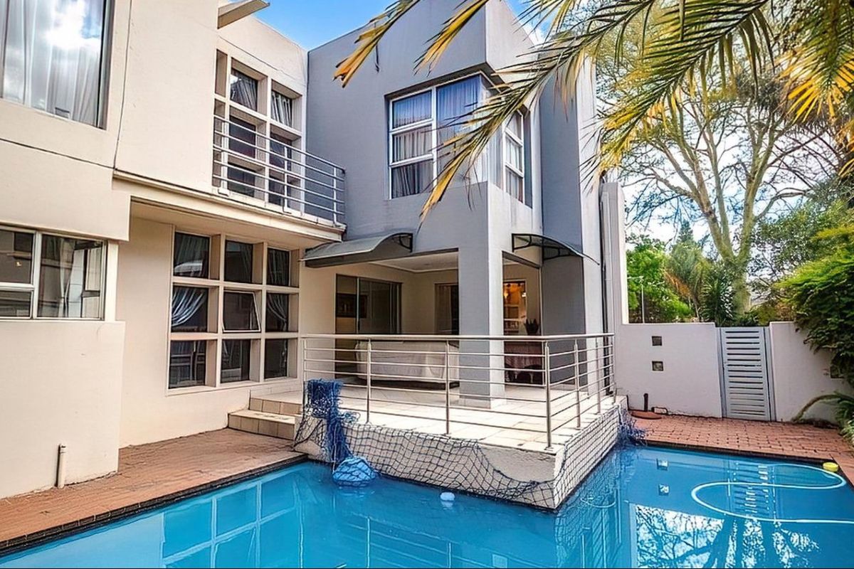 Rear exterior view featuring a swimming pool, paved deck area, and a covered patio with stainless steel balustrades.