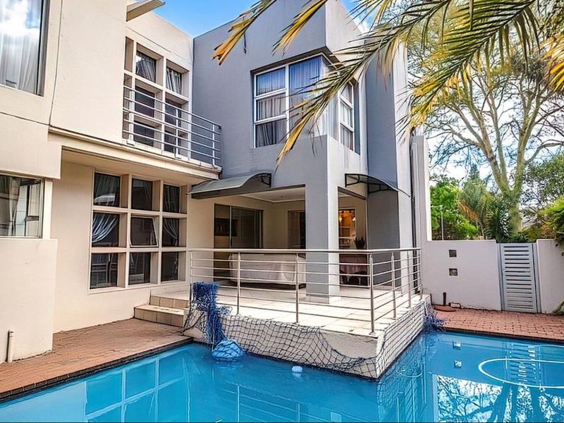 Rear exterior view featuring a swimming pool, paved deck area, and a covered patio with stainless steel balustrades.