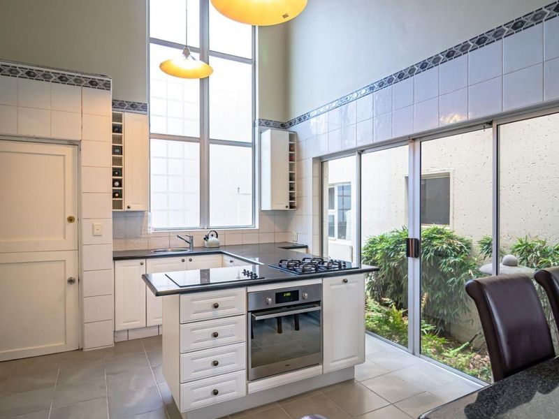 A bright kitchen featuring double-height ceilings, white cabinetry, granite countertops, a central island with a gas hob and oven, and sliding doors to a garden.