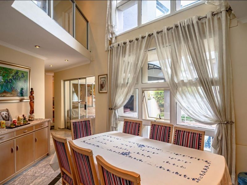 Spacious dining area featuring double volume ceilings, large windows for natural light, and a mezzanine level with a modern glass balustrade.