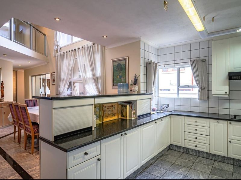 Spacious open-plan kitchen and dining area featuring built-in cabinetry, granite countertops, and a double-volume ceiling with a mezzanine level overlooking the living space.