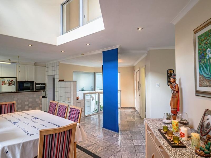 Spacious open-plan living and dining area featuring tiled floors, a double-volume ceiling with a skylight, and an integrated kitchen with built-in cabinetry.