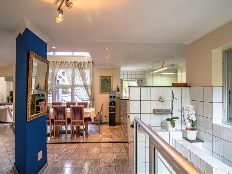 An open-plan living and dining area featuring tiled flooring, a central blue feature pillar, and a tiled partition wall separating the kitchen space.