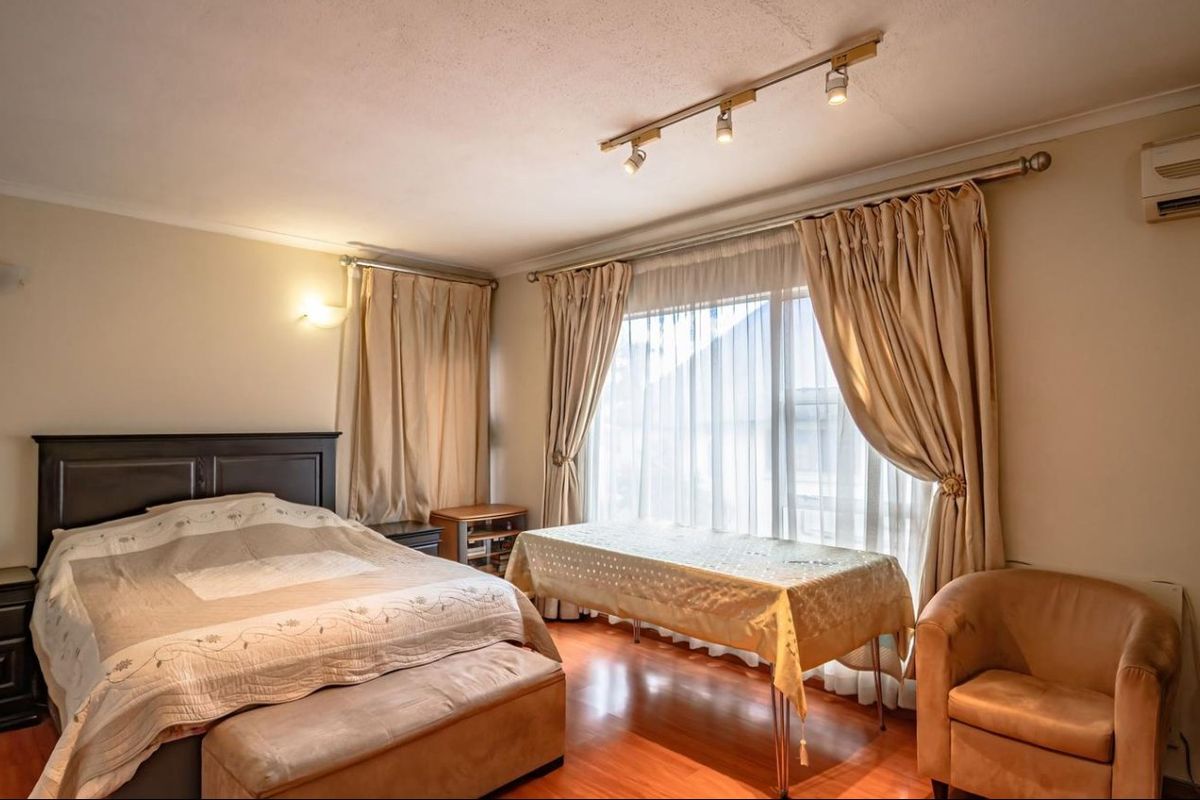 A spacious bedroom featuring laminate flooring, wall-mounted air conditioning, and ample natural light through large windows with fitted curtain rods.