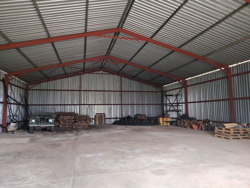 A spacious, open-plan utility shed or barn featuring a robust steel frame, corrugated metal cladding, and a durable concrete floor.