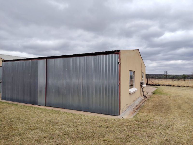 Rear view of a farm outbuilding featuring corrugated metal cladding, steel-framed windows, and a concrete apron foundation.