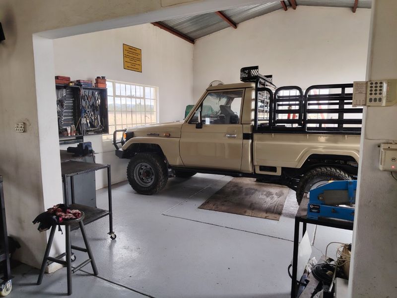 A functional garage space featuring painted concrete flooring, exposed roof trusses, and wall-mounted tool storage, suitable for vehicle maintenance or storage.