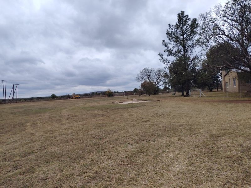 Expansive open farm land featuring mature trees, perimeter fencing, and overhead power lines under a cloudy sky.