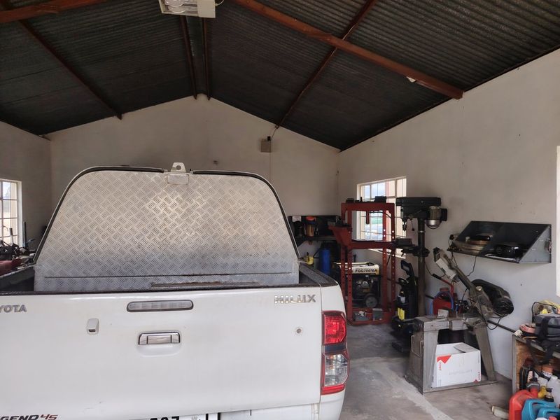 A functional farm garage featuring exposed timber roof trusses, corrugated metal roofing, and concrete flooring, currently utilized as a workshop space.