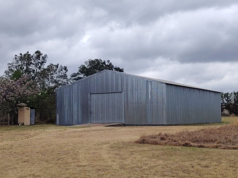 A large, functional corrugated metal farm shed or barn featuring a wide sliding entrance door, set on a rural property.