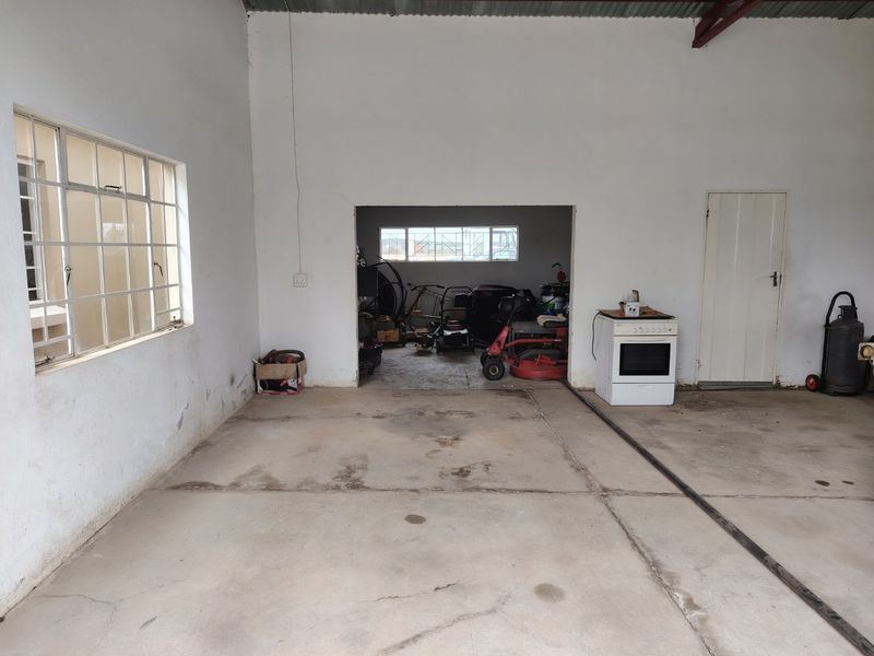 A spacious utility area featuring a concrete floor, steel-framed windows, and a built-in oven, offering versatile potential for storage or workshop use.