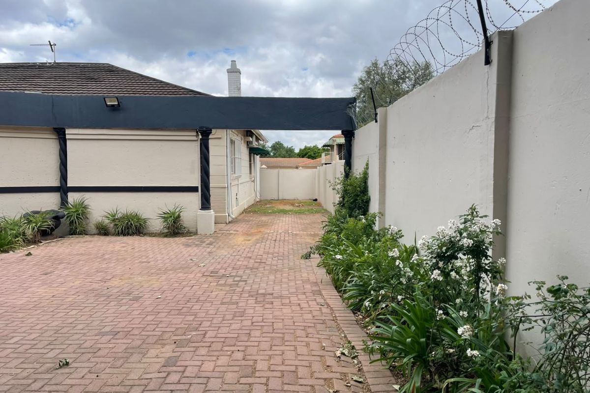 Rear exterior area featuring a paved driveway, perimeter wall with security razor wire, and decorative structural pillars.