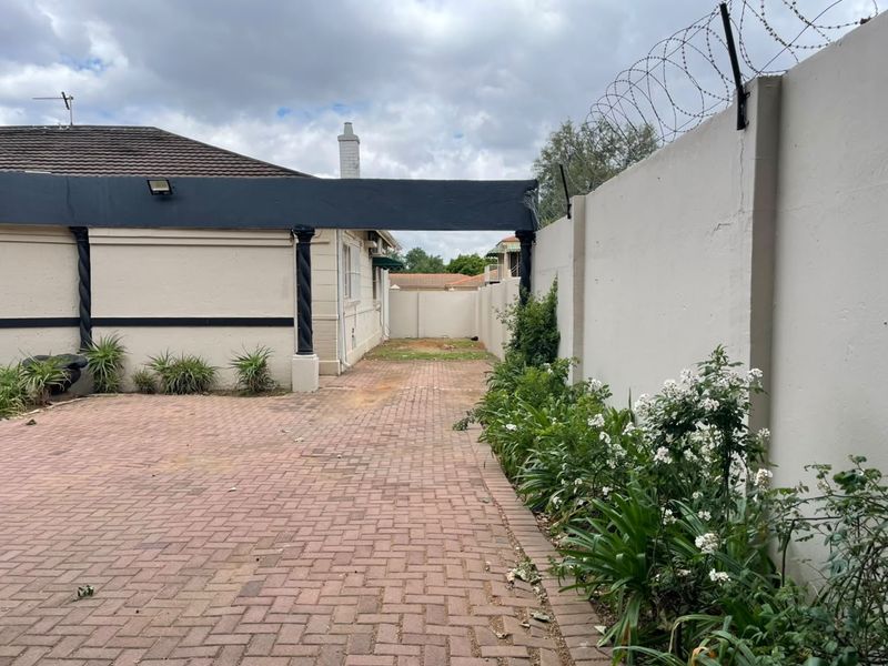 Rear exterior area featuring a paved driveway, perimeter wall with security razor wire, and decorative structural pillars.