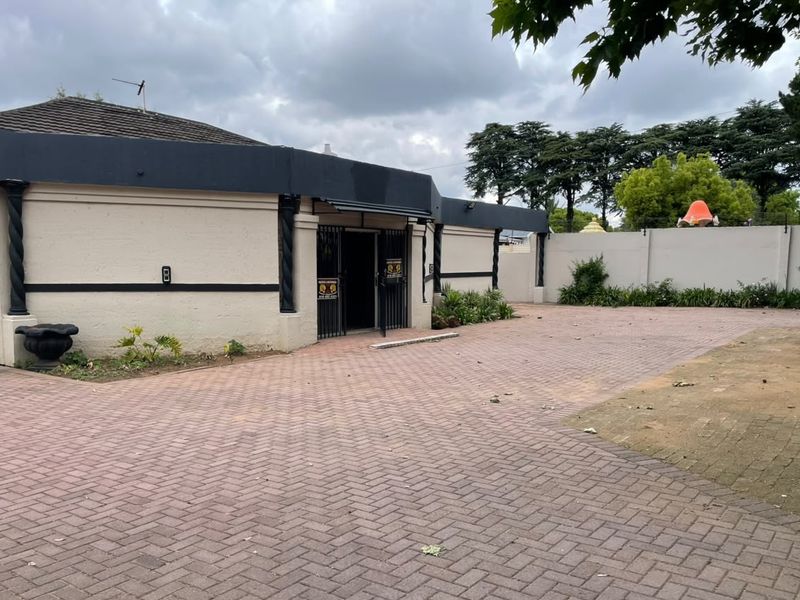 Front exterior view of a commercial property featuring a paved driveway, perimeter wall, and security gate entrance.