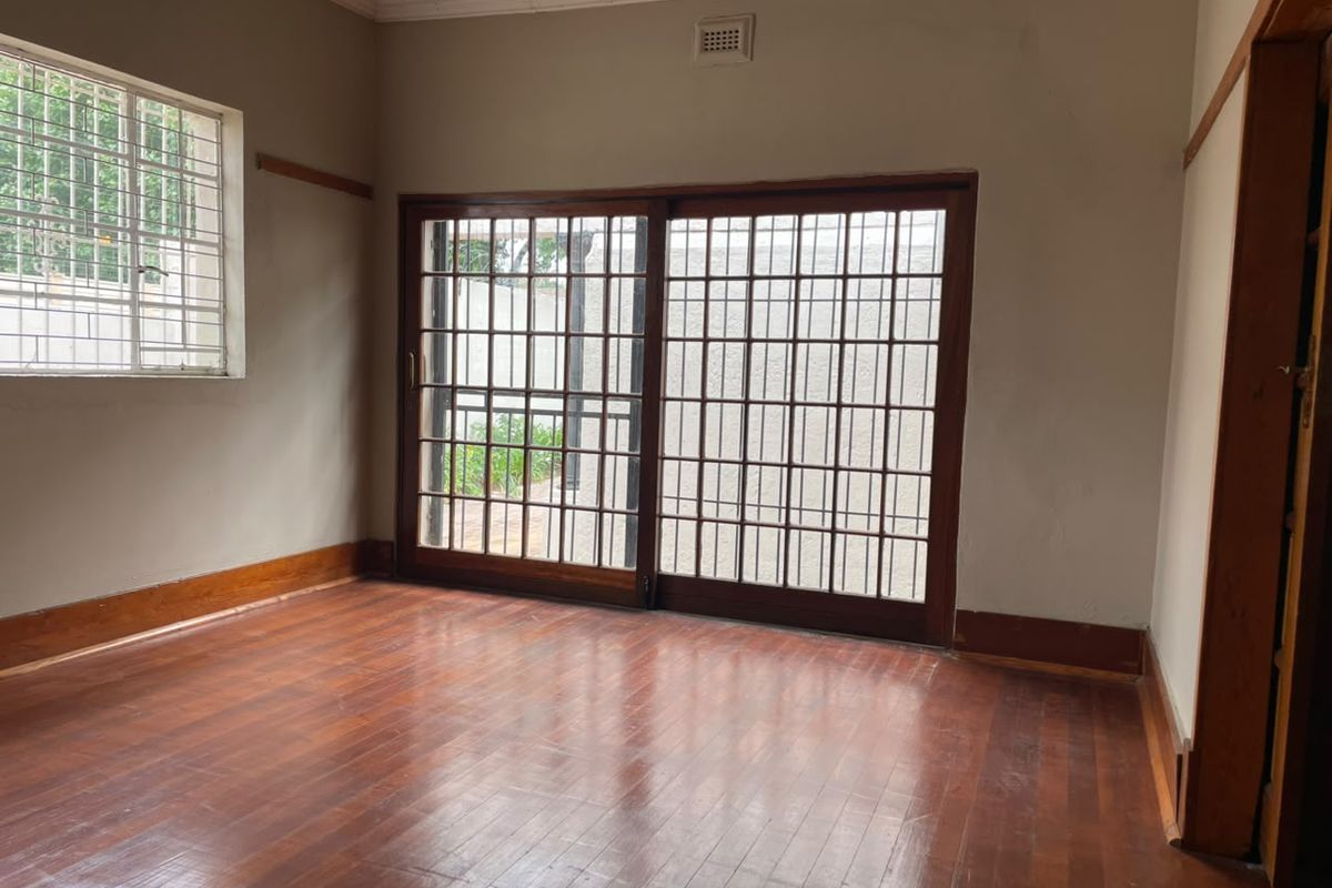 An empty living room featuring polished hardwood flooring, crown molding, and large sliding glass doors with security bars providing access to the exterior.