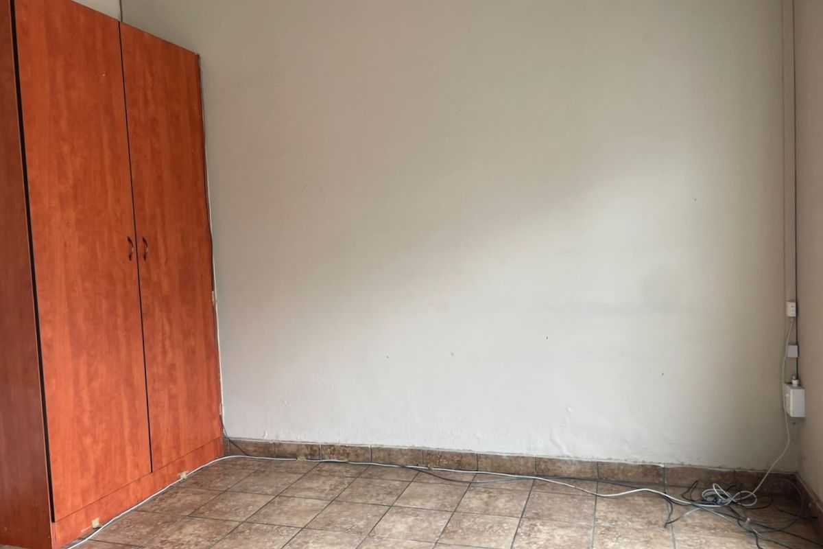 A simple bedroom featuring tiled flooring and a built-in wooden wardrobe, offering a blank canvas for customization.