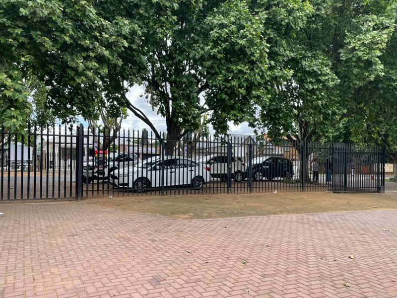 Front exterior view of the commercial property featuring paved driveway access and secure metal perimeter fencing shaded by mature trees.