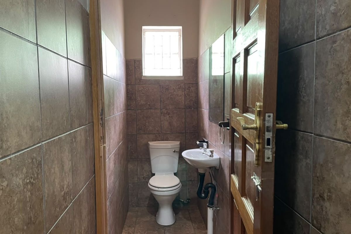 A compact guest bathroom featuring full-height ceramic wall tiling, a wall-mounted basin, and a standard toilet with exposed plumbing.