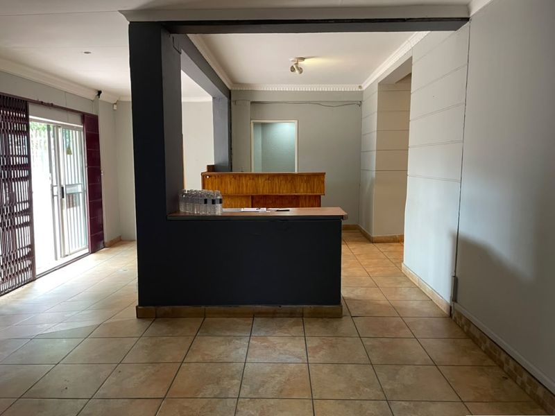 Open-plan commercial space featuring a built-in reception counter, tiled flooring, and a secure sliding glass entrance.