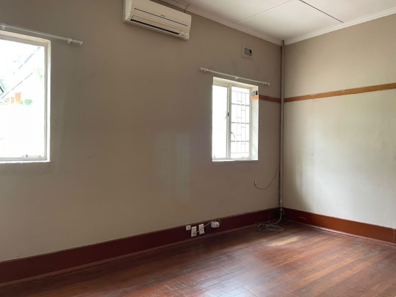 An empty office space featuring timber flooring, split-system air conditioning, and security-barred windows, suitable for a professional workspace.