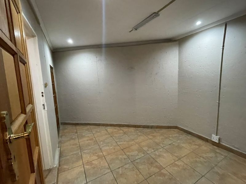 An empty utility space featuring tiled flooring, recessed downlights, and exposed electrical conduit, suitable for storage or a functional workspace.