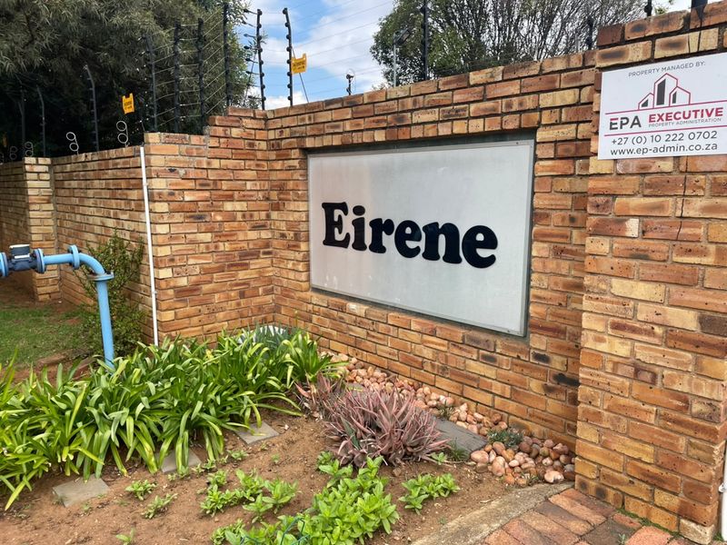 Entrance signage for Eirene complex featuring a brick boundary wall with integrated electric fencing and a landscaped garden bed.