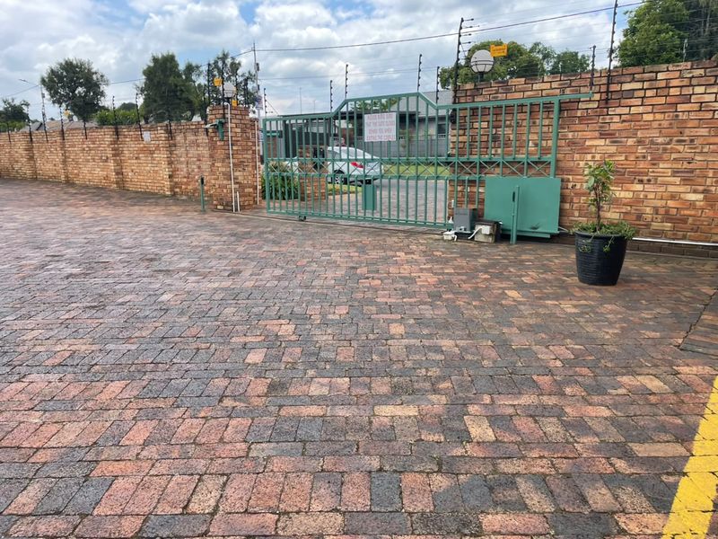 Front entrance of the townhouse complex featuring a secure sliding gate, brick boundary wall with electric fencing, and a paved driveway.