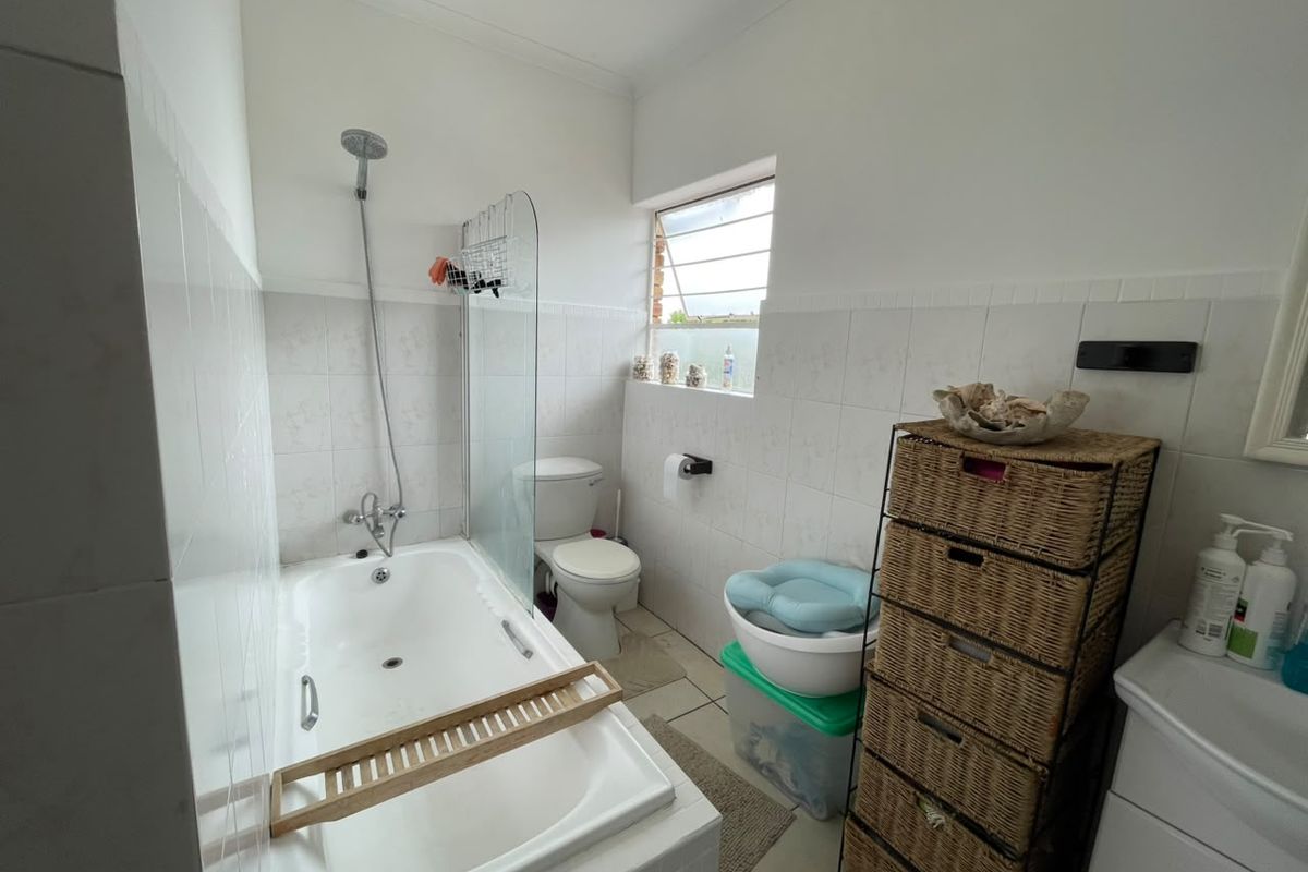 A functional bathroom featuring a combined bathtub and shower, tiled walls, and a louver window for ventilation.