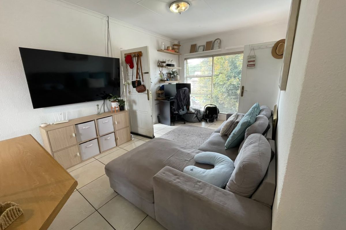A compact living room featuring tiled flooring, a ceiling light fixture, and a window with blinds, offering a functional space for relaxation.