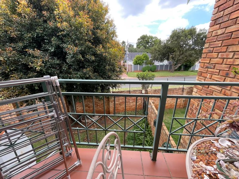 A balcony featuring tiled flooring and a metal balustrade, overlooking a private garden area and street view.