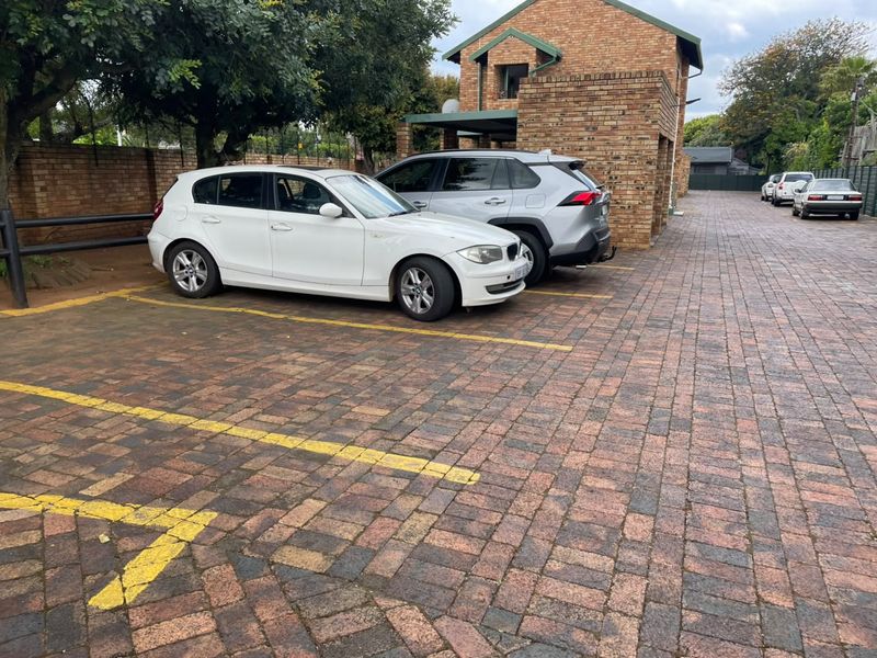 Exterior view of the townhouse complex parking area featuring paved driveway, designated parking bays, and face-brick building facade.