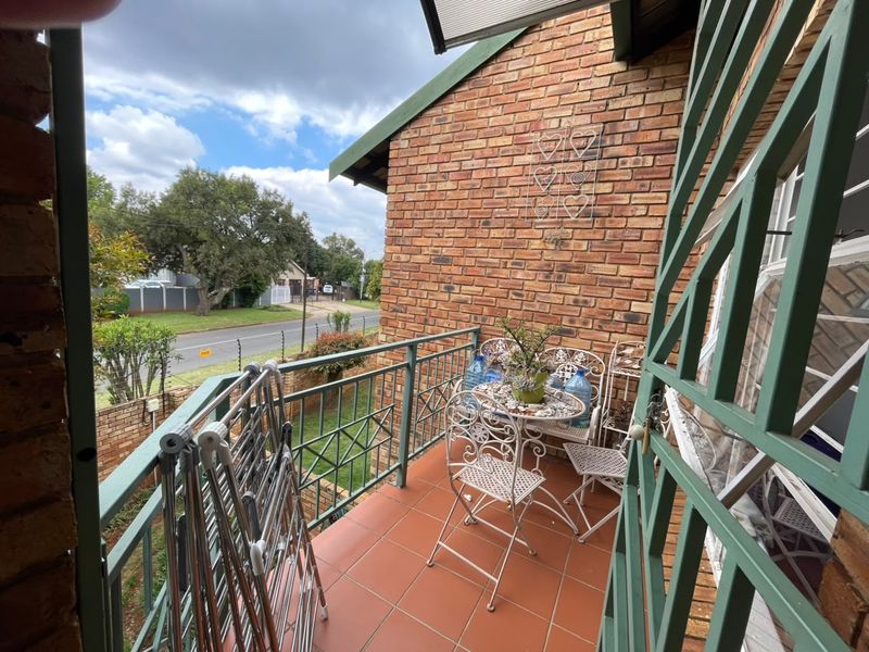 A covered balcony featuring tiled flooring, exposed brick walls, and a metal balustrade, offering an outdoor space with views of the street.