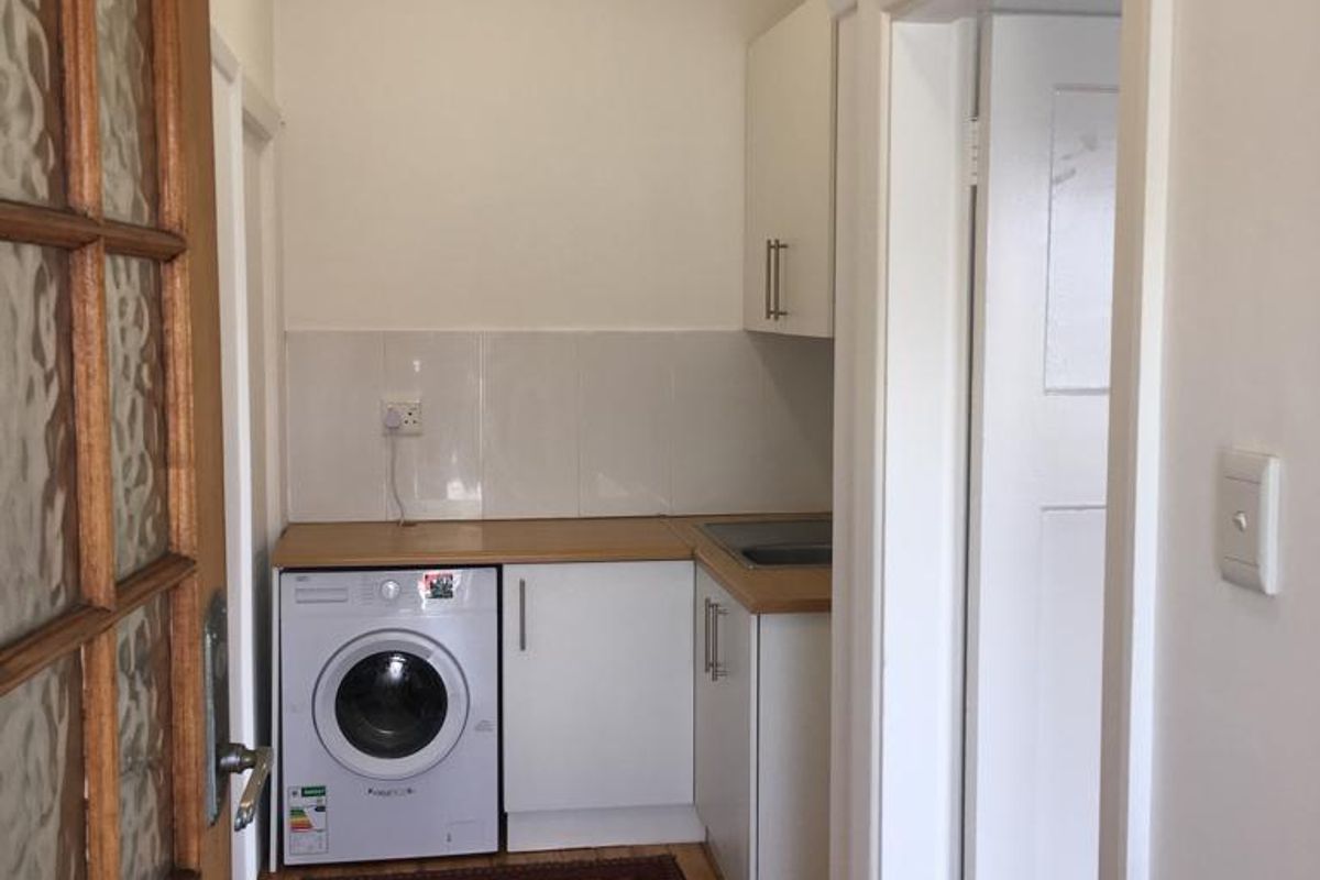 A compact laundry area featuring built-in white cabinetry, a laminate countertop, tiled splashback, and timber flooring.