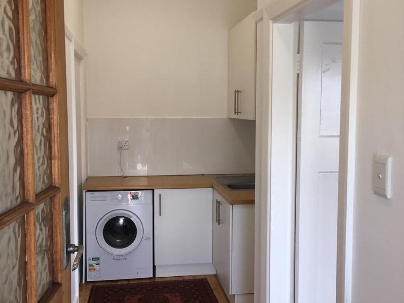 A compact laundry area featuring built-in white cabinetry, a laminate countertop, tiled splashback, and timber flooring.