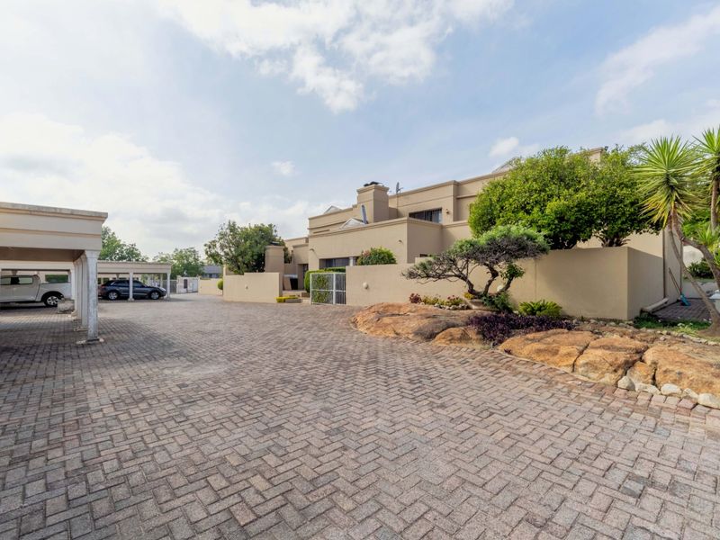 A well-maintained exterior view of the property featuring a paved driveway, covered carport parking, and established landscaped garden areas.