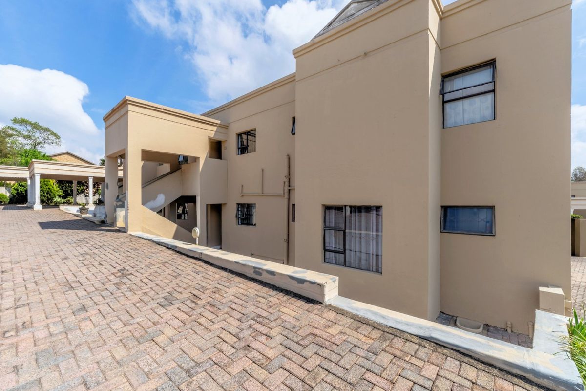 Rear exterior view of the apartment building featuring a paved driveway, concrete retaining wall, and multi-level access staircase.