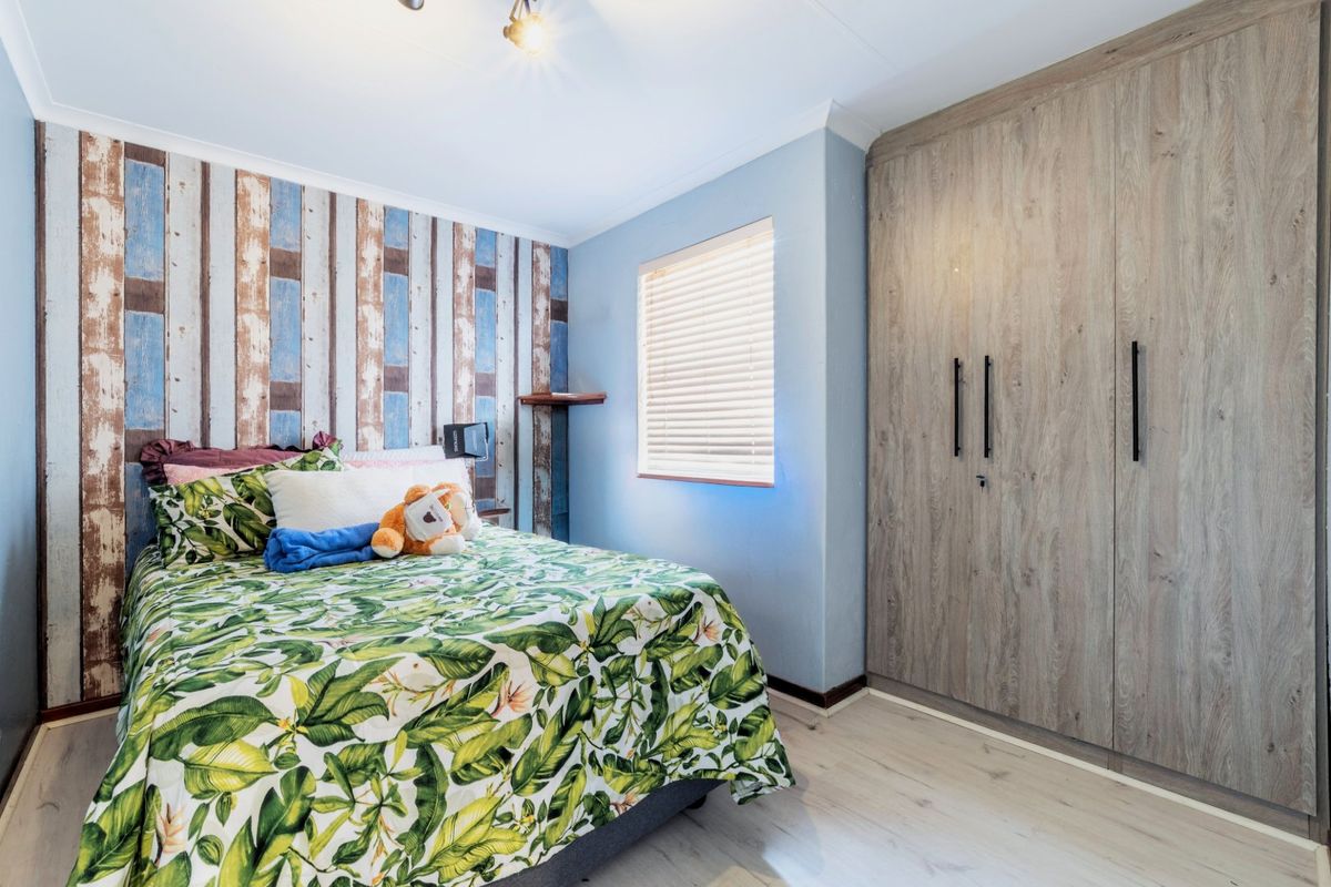 A well-maintained bedroom featuring light wood-look laminate flooring, a large built-in wardrobe with wood-grain finish, and venetian blinds.