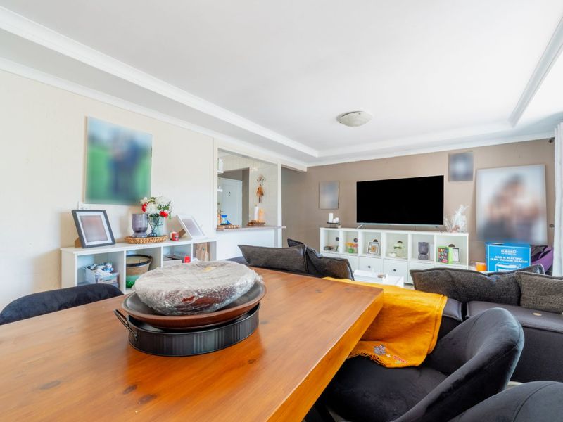 Open-plan living and dining area featuring a pass-through window to the kitchen and decorative ceiling cornicing.
