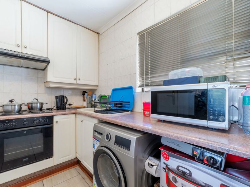 A compact kitchen featuring built-in cabinetry, a tiled backsplash, integrated oven and hob, and a dedicated space for laundry appliances.