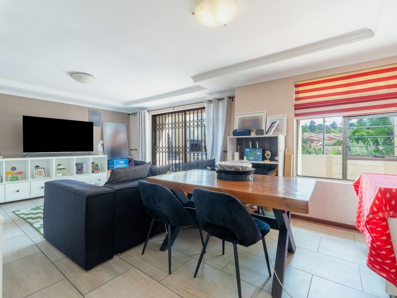 Open plan living and dining area featuring tiled flooring, large windows with security bars, and a sliding door leading to an outdoor space.