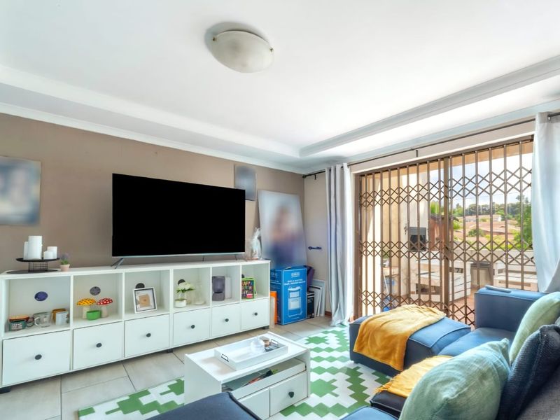 A comfortable living room featuring tiled flooring, a decorative cove ceiling, and a sliding glass door with a security gate leading to the patio.