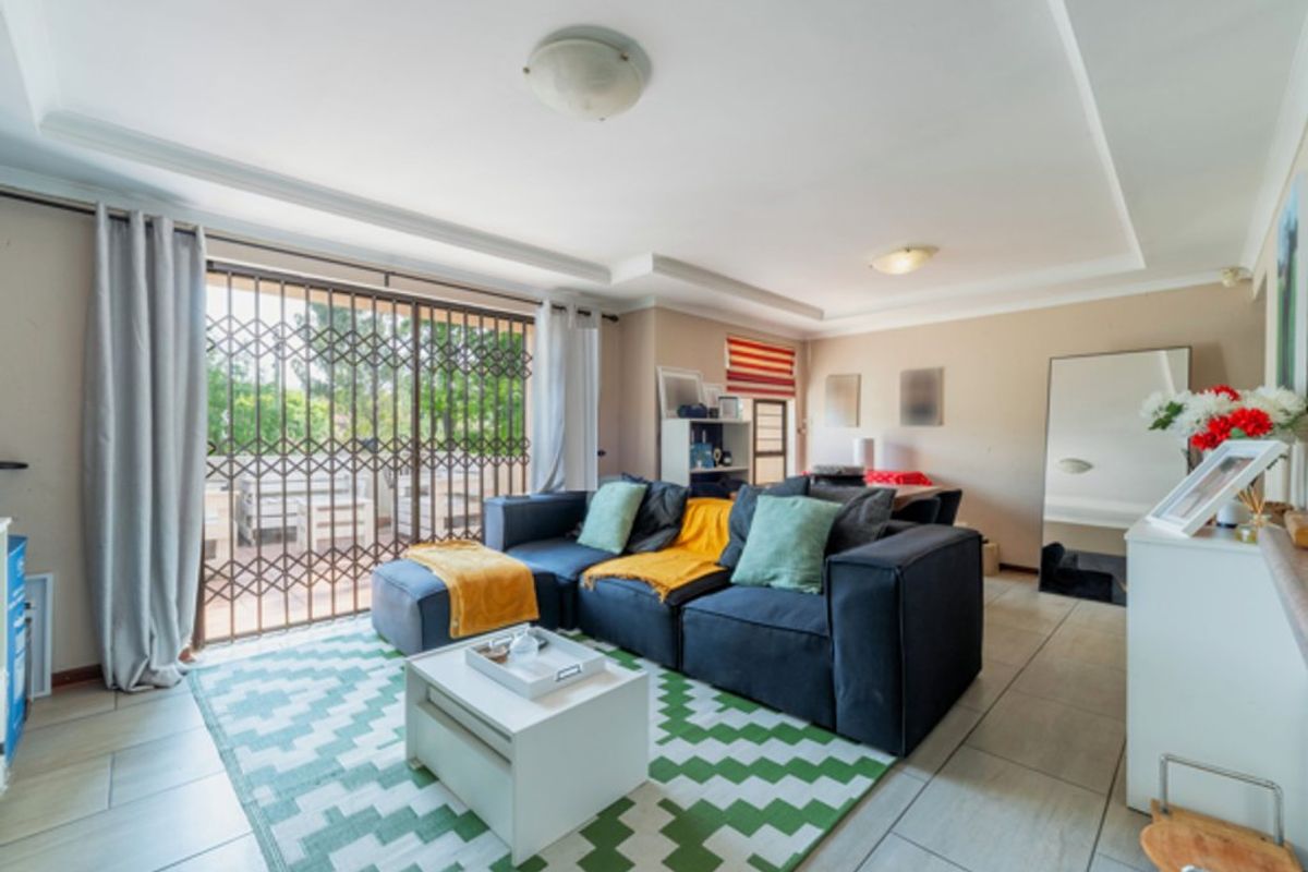 A bright living room featuring tiled flooring, recessed ceiling details, and a sliding glass door with a security gate leading to the patio.