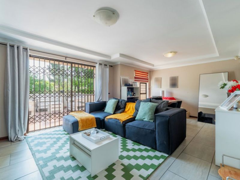 A bright living room featuring tiled flooring, recessed ceiling details, and a sliding glass door with a security gate leading to the patio.