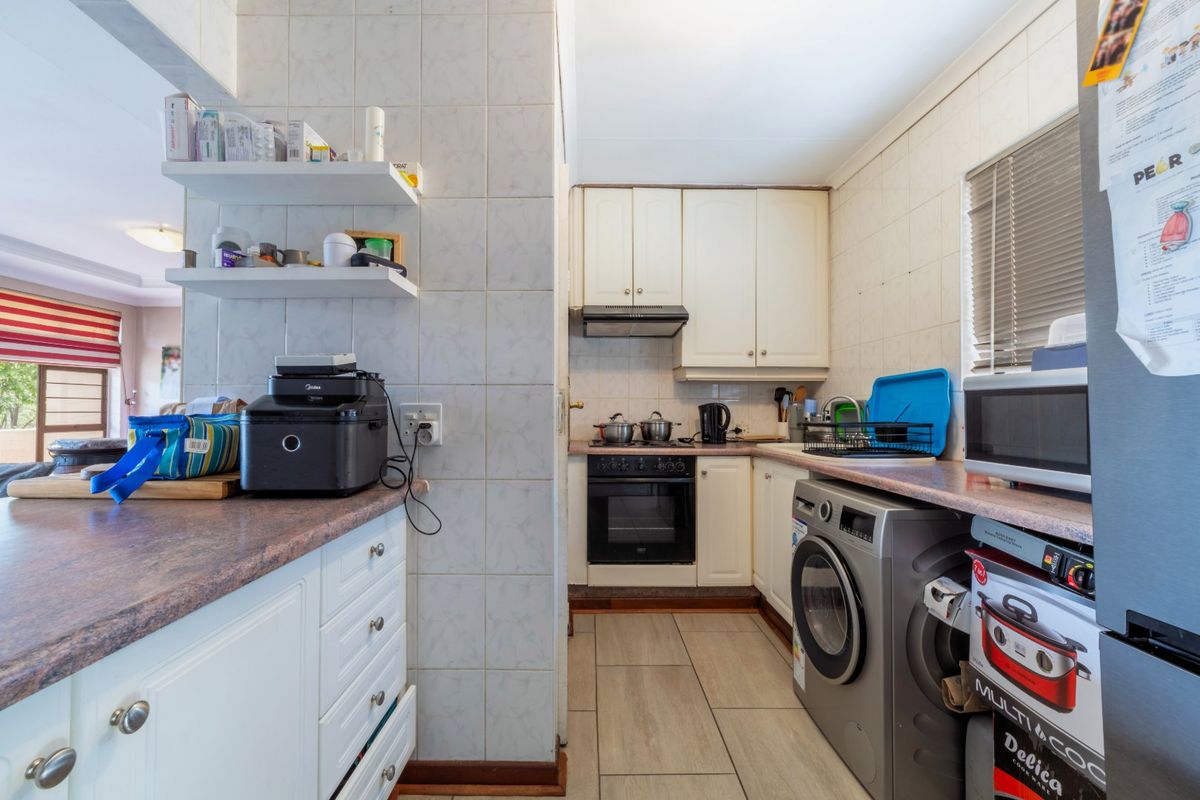 Compact kitchen featuring white cabinetry, laminate countertops, built-in oven and hob, and tiled finishes, providing a functional workspace with integrated laundry plumbing.