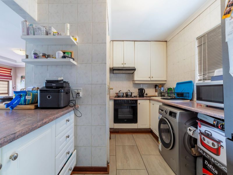 Compact kitchen featuring white cabinetry, laminate countertops, built-in oven and hob, and tiled finishes, providing a functional workspace with integrated laundry plumbing.